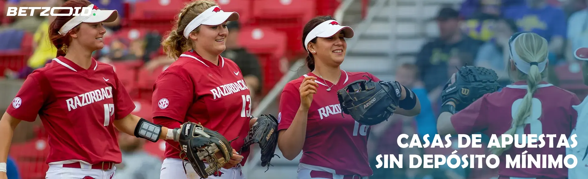 Tres jugadoras con uniformes rojos y guantes de béisbol en el campo.