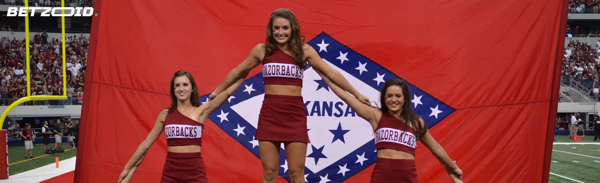 Cheerleaders in front of the Arkansas flag.