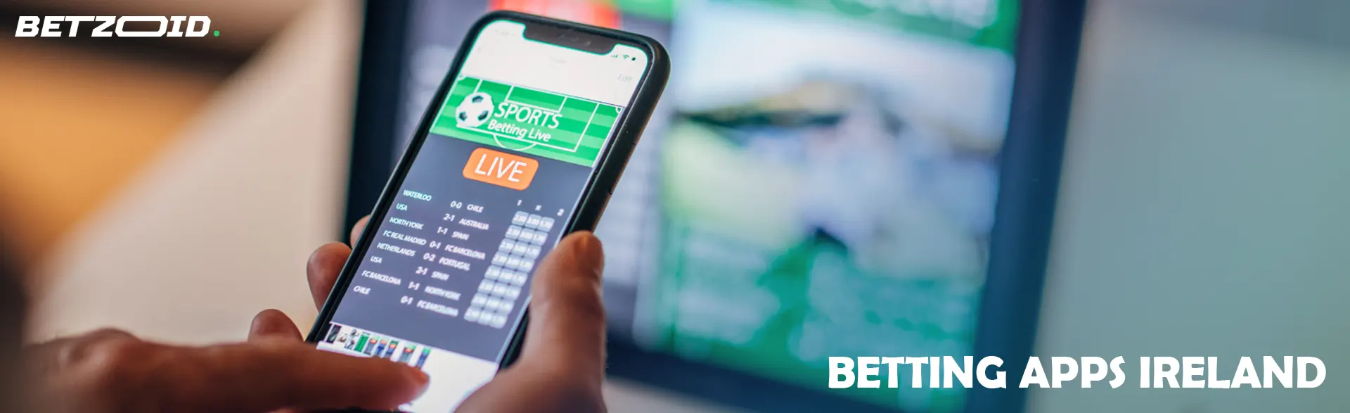 Man holding smartphone with betting app near computer.