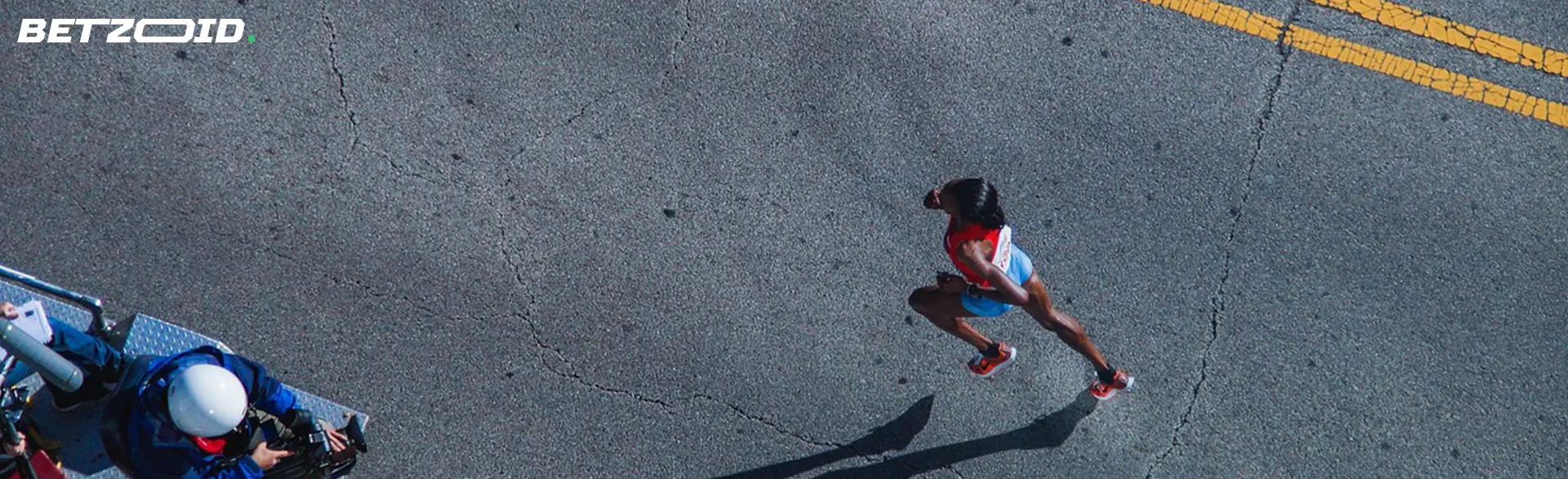 An overhead view of a runner sprinting on a road, with a cameraman capturing the moment.