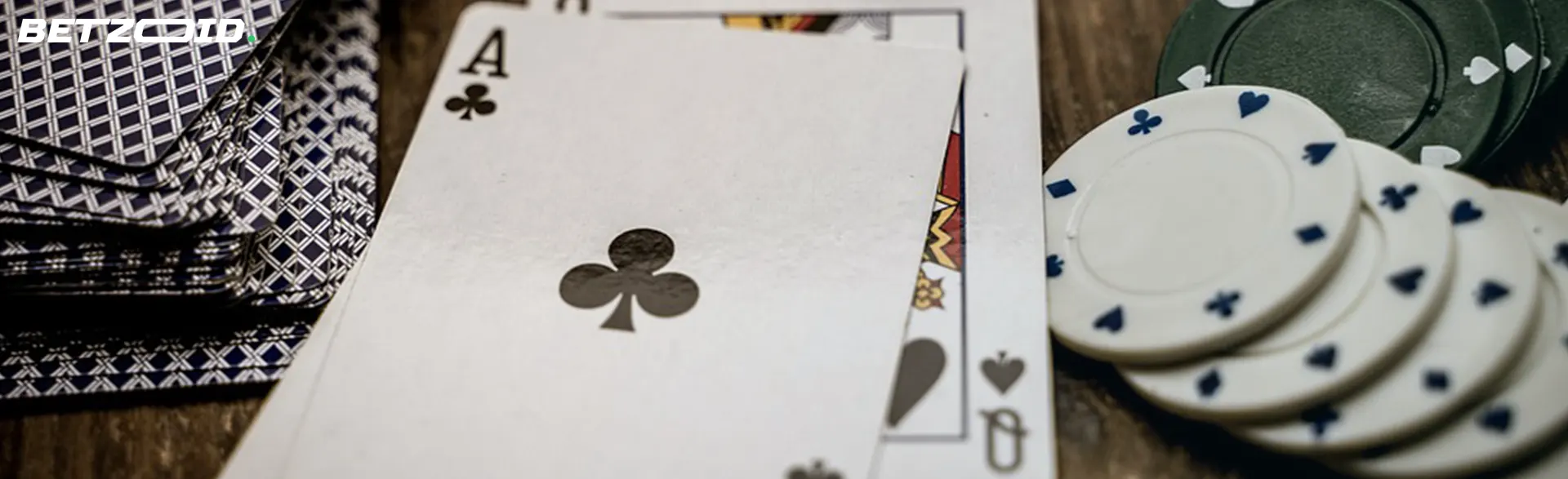 Close-up of an ace of clubs card beside a deck and poker chips on a wooden table.
