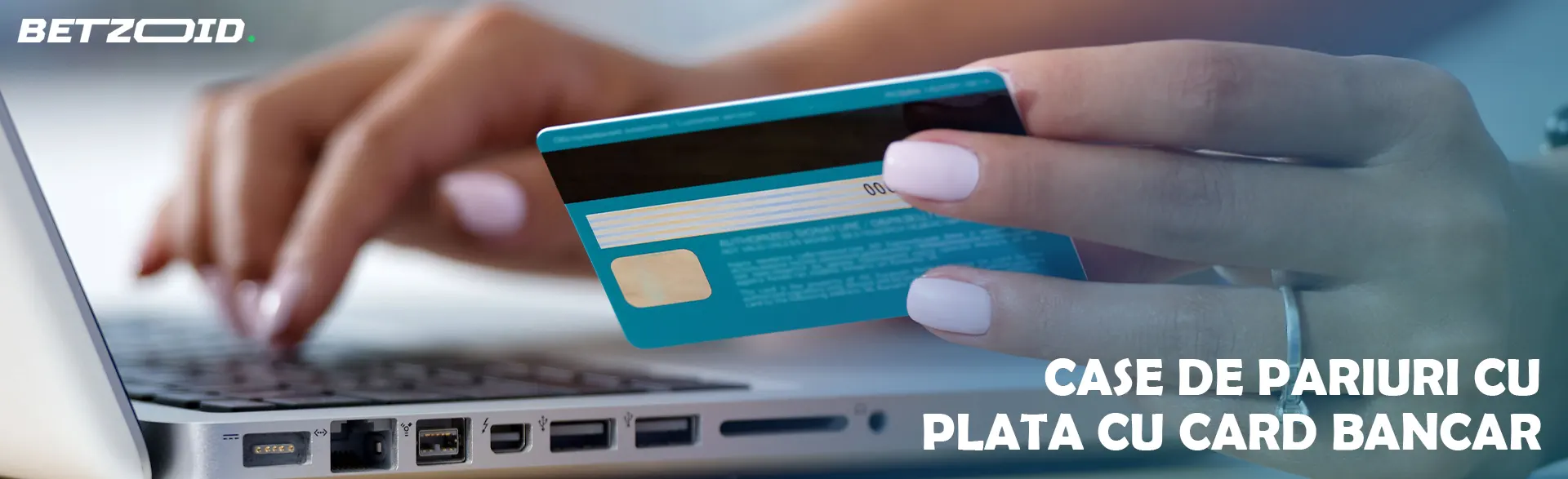 O femeie ține un card bancar în mână lângă un laptop.