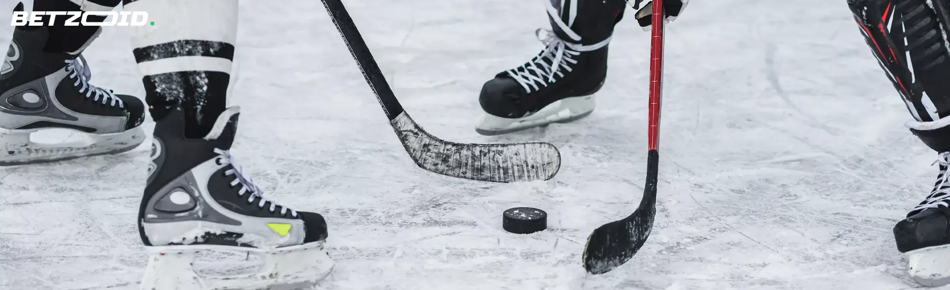 Hokejisté bojují o puk hokejkami.