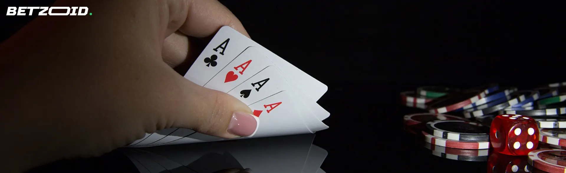 Una mano tiene quattro assi mentre sullo sfondo si vedono fiches da casinò e un dado rosso.