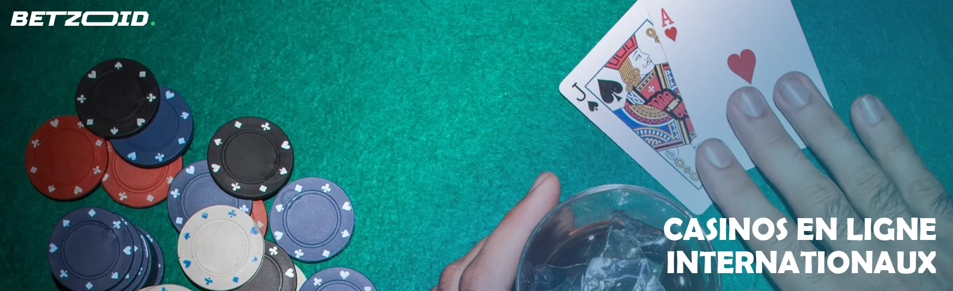 Un joueur tient des cartes à côté des jetons de casino et une boisson dans un verre.