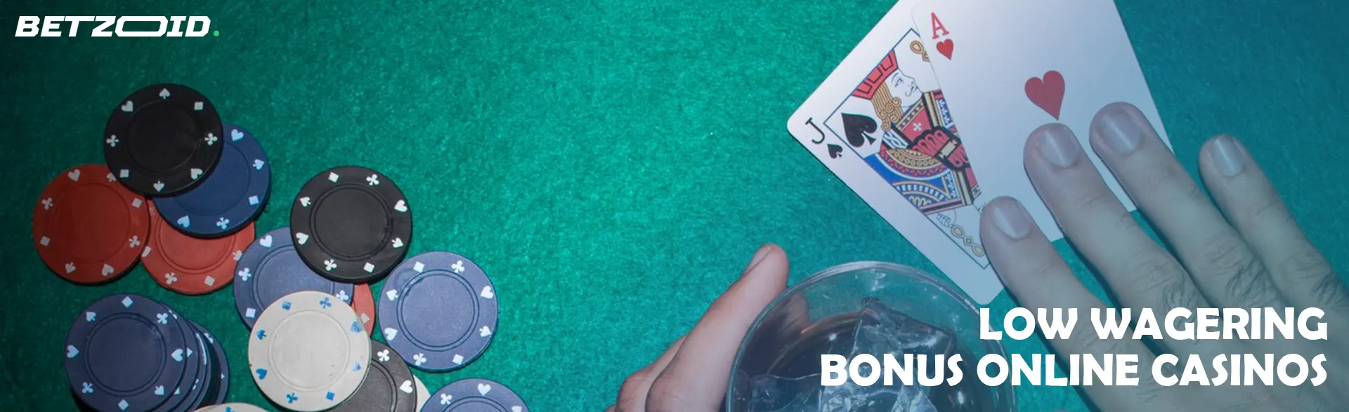 A player holds cards next to casino chips and a drink in a glass.