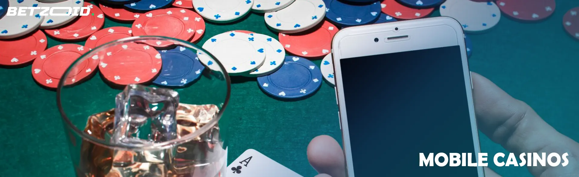 A smartphone in the hands of a player next to casino chips and a drink in a glass.