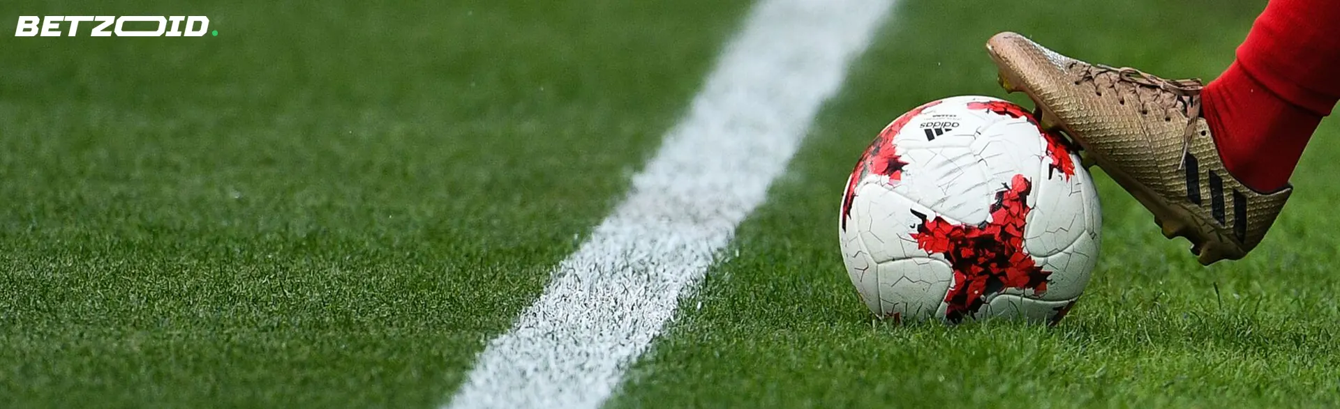 A football player keeps the ball on the grass with his foot.