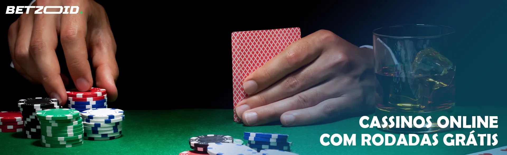 Um jogador segura cartas ao lado de fichas de cassino e uma bebida em um copo.