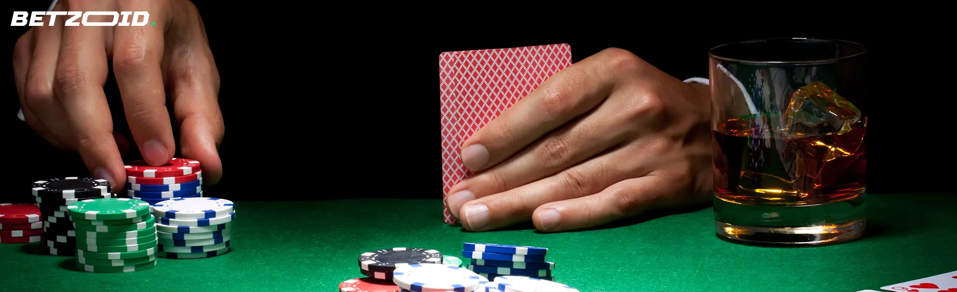 A player holds cards next to casino chips and a drink in a glass.
