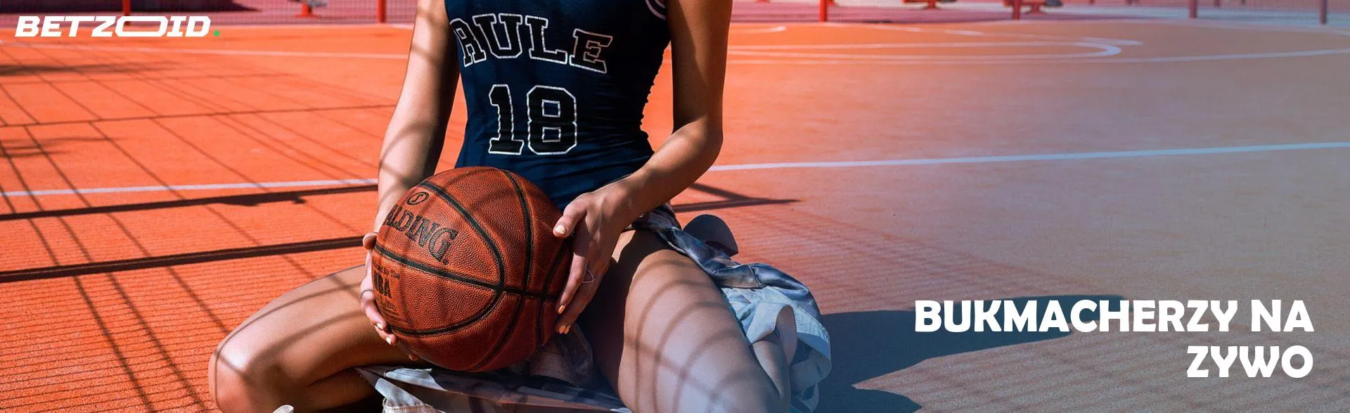 Koszykarz siedzi z piłką na boisku.